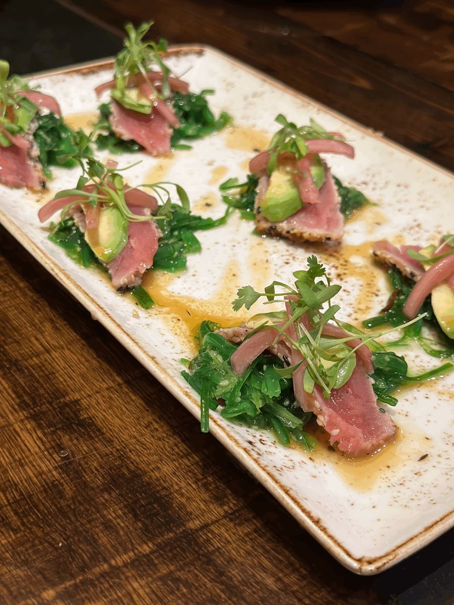 Seared ahi tataki with pickled onion, avocado and micro greens on a long plate