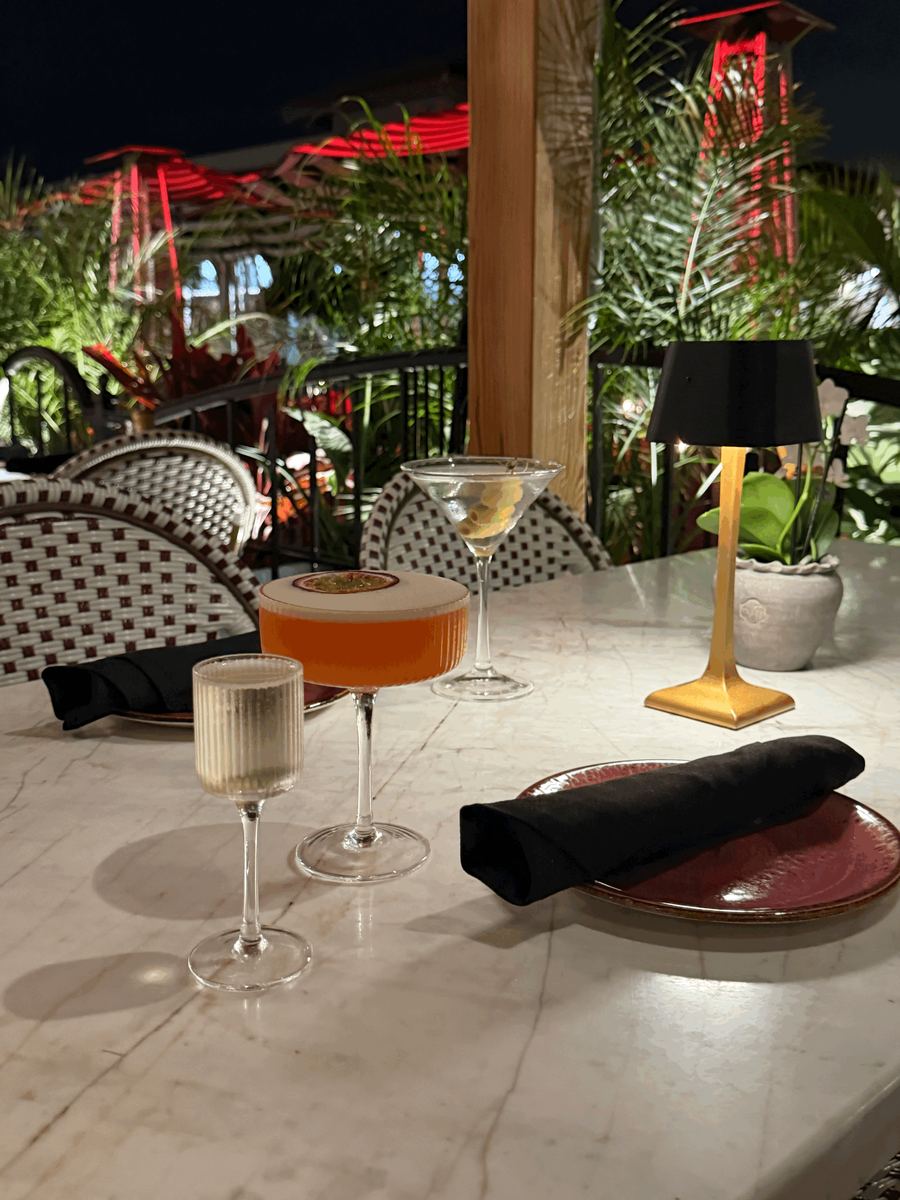 A passion fruit martini and a classic martini on a marble patio table at night, heat lamps glowing behind